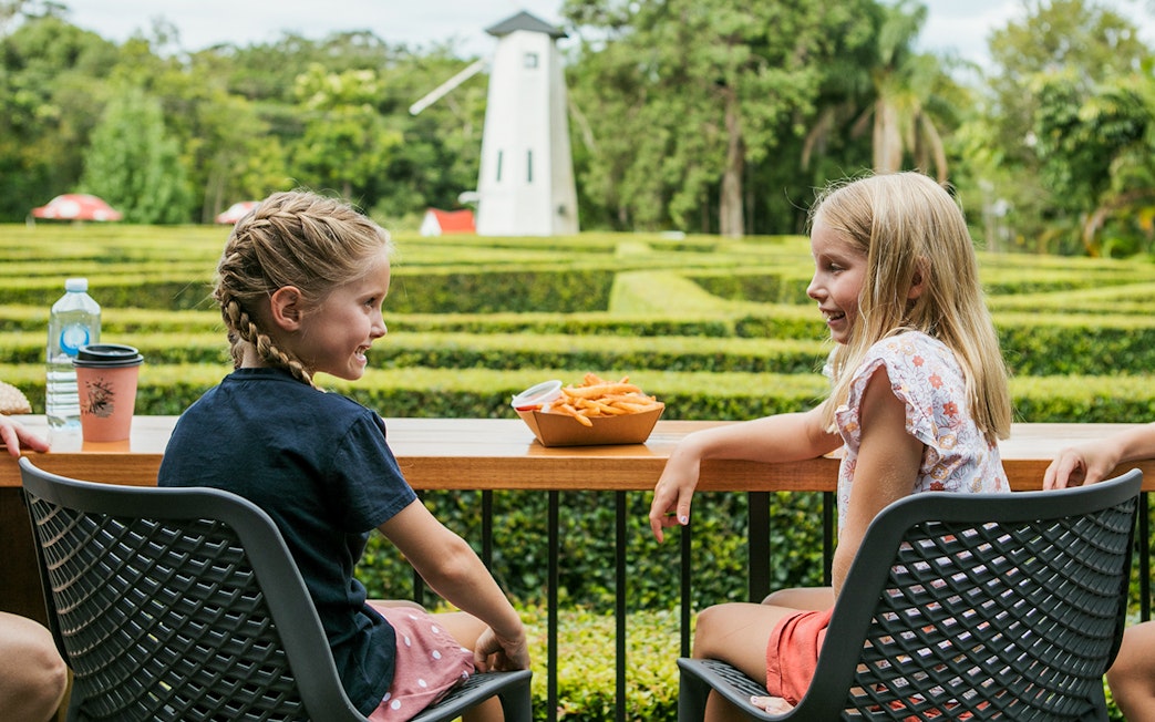 Children enjoying snacks at a table with a hedge maze and windmill in Amaze World.