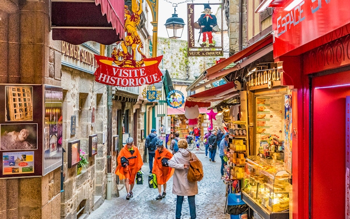 Narrow street in Mont Saint-Michel with tourists and historic shop signs.