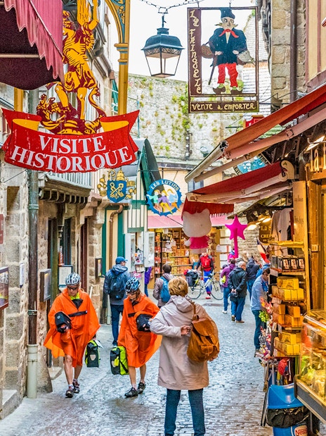 Narrow street in Mont Saint-Michel with tourists and historic shop signs.