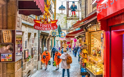 Narrow street in Mont Saint-Michel with tourists and historical signs, part of audio-guided tour.