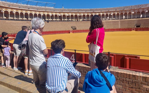 Visitors on a guided tour of the Seville Bullring, observing the arena and seating.