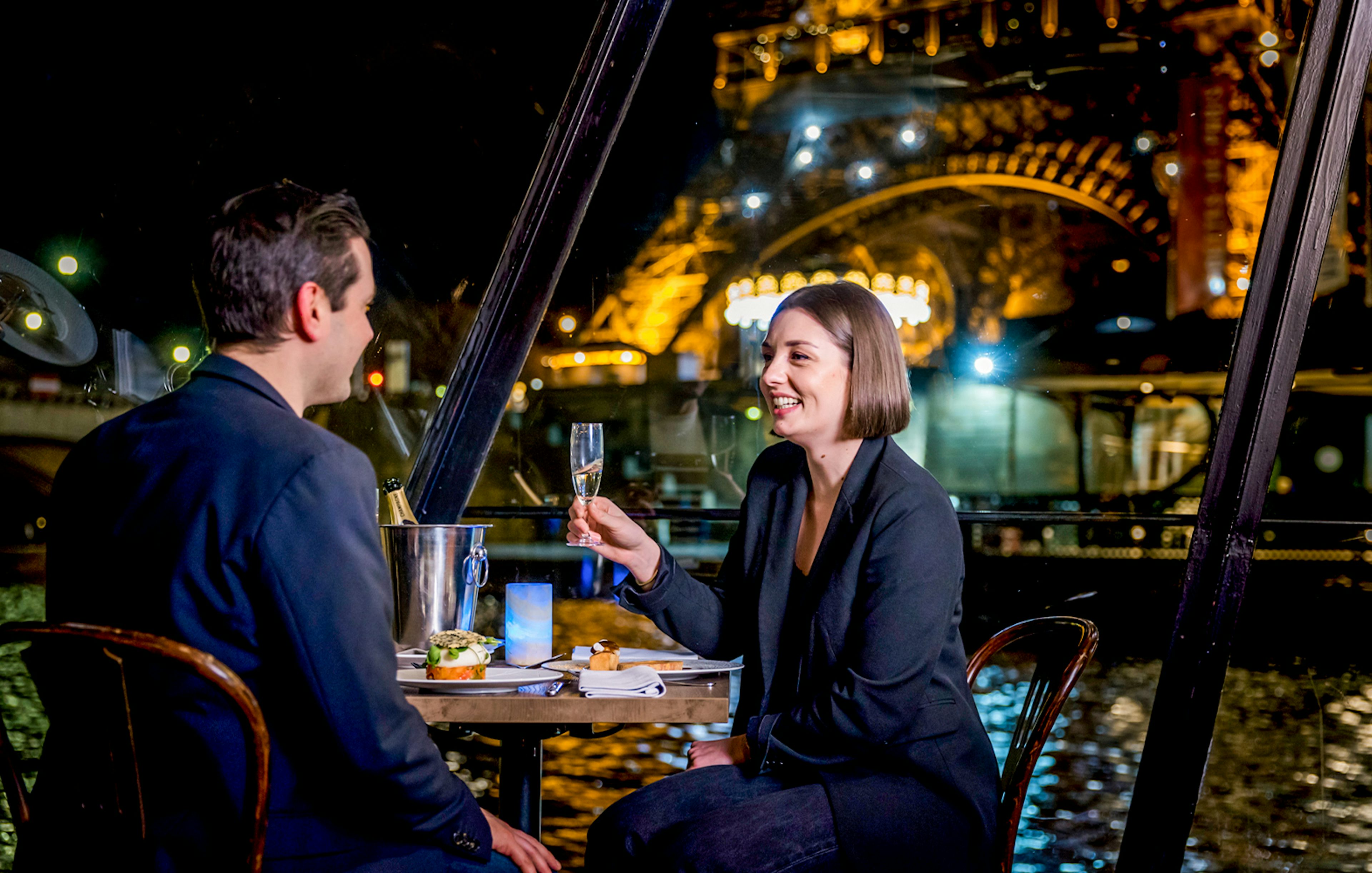 Couple enjoying dinner on Seine River cruise with Eiffel Tower view.