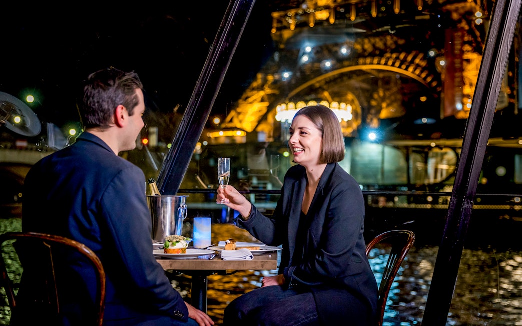 Couple enjoying dinner on Seine River cruise with Eiffel Tower view.