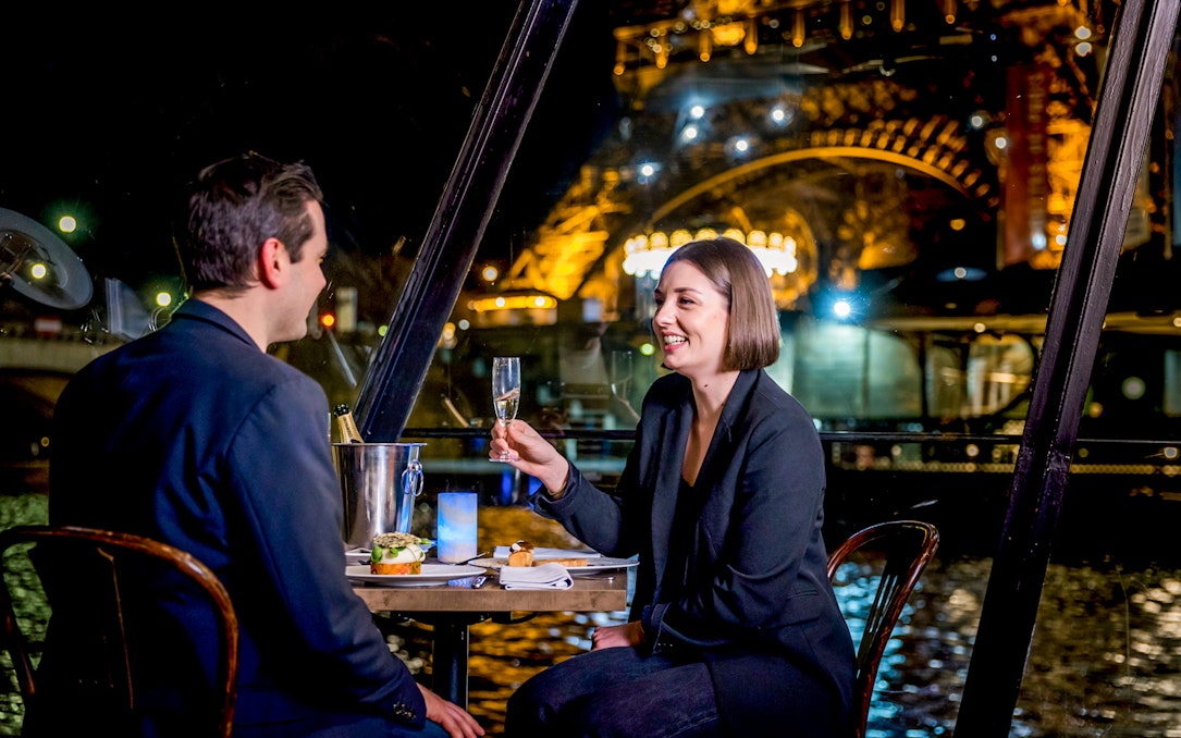 Couple enjoying dinner on Seine River cruise with Eiffel Tower view.