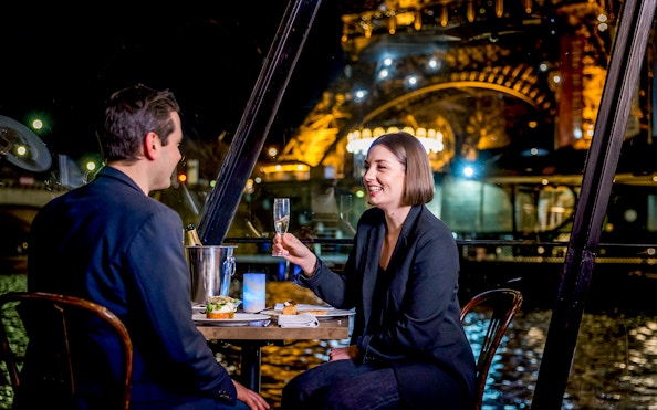 Couple enjoying dinner on Seine River cruise with Eiffel Tower view.