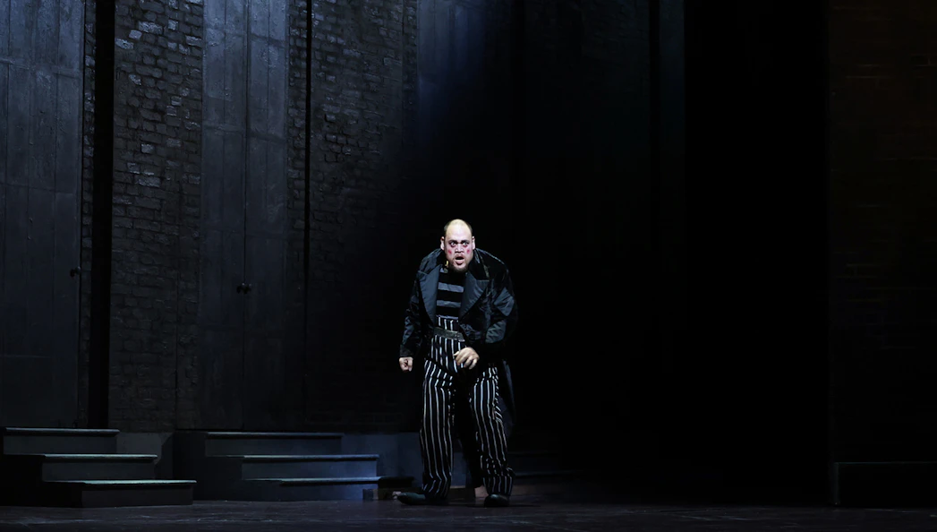 Performer in striped costume on stage during Rigoletto opera.