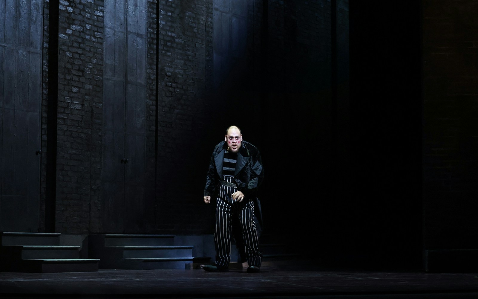 Performer in striped costume on stage during Rigoletto opera.
