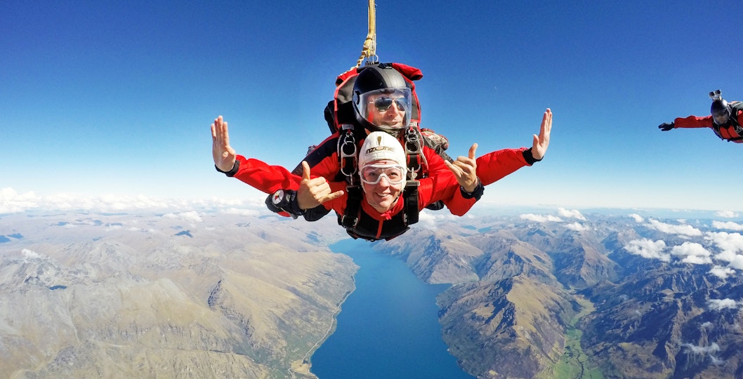 Tandem skydivers over Lake Wakatipu, Queenstown, with mountain views.