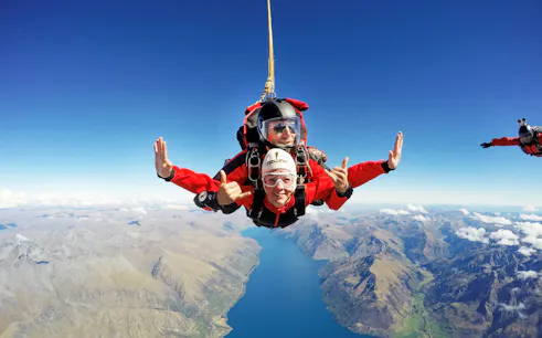 Tandem skydivers over Lake Wakatipu, Queenstown, with mountain views.