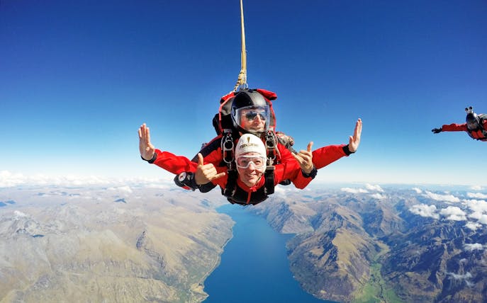 Tandem skydivers over Lake Wakatipu, Queenstown, with mountain views.