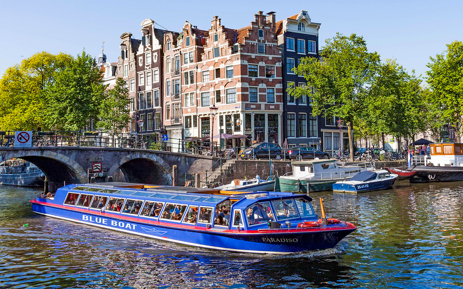 Amsterdam canal tour boat cruising under a historic bridge on the Blue Boat Cruise.