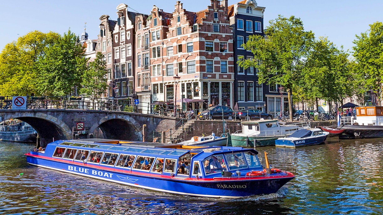 Amsterdam canal tour boat cruising under a historic bridge on the Blue Boat Cruise.
