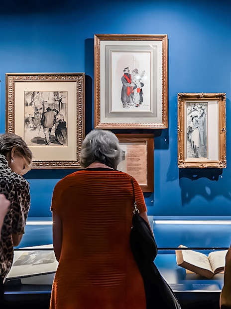 Visitors viewing framed art and documents at the Montmartre Museum exhibit.