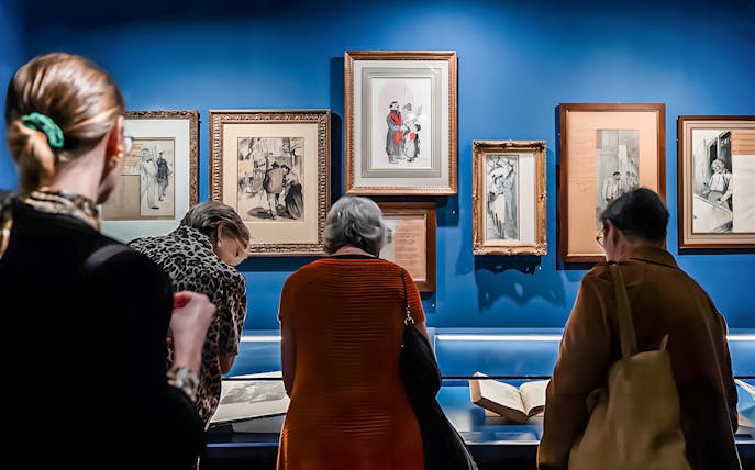 Visitors viewing framed art and documents at the Montmartre Museum exhibit.