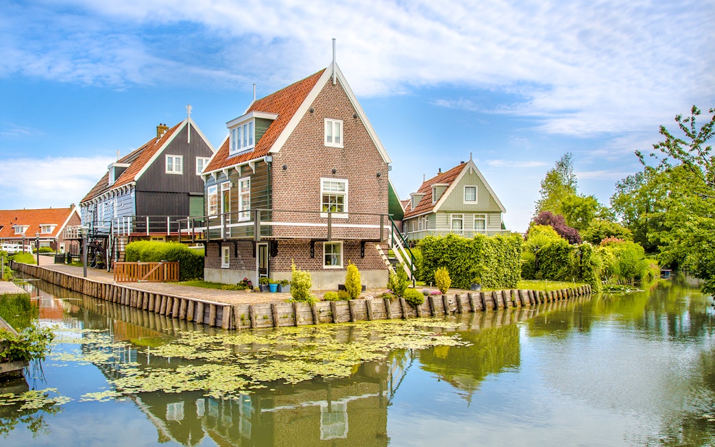 Marken fisherman's houses by a canal with greenery and blue sky.