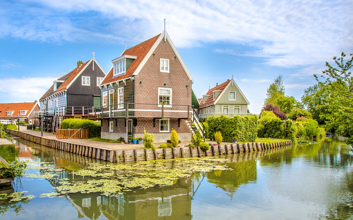 Marken fisherman's houses by a canal with greenery and blue sky.