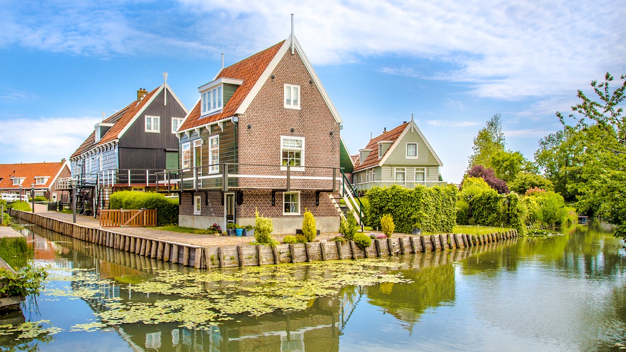 Marken fisherman's houses by a canal with greenery and blue sky.