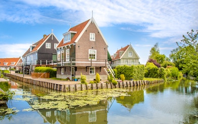 Marken fisherman's houses by a canal with greenery and blue sky.