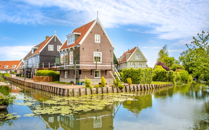 Marken fisherman's houses by a canal with greenery and blue sky.