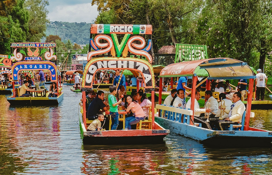 Trajinera boat with colorful decorations on Xochimilco canal, Mexico City, featuring lively group celebration.