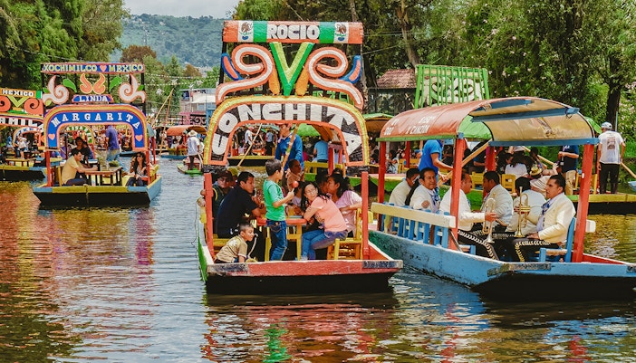 Trajinera boat with colorful decorations on Xochimilco canal, Mexico City, featuring lively group celebration.