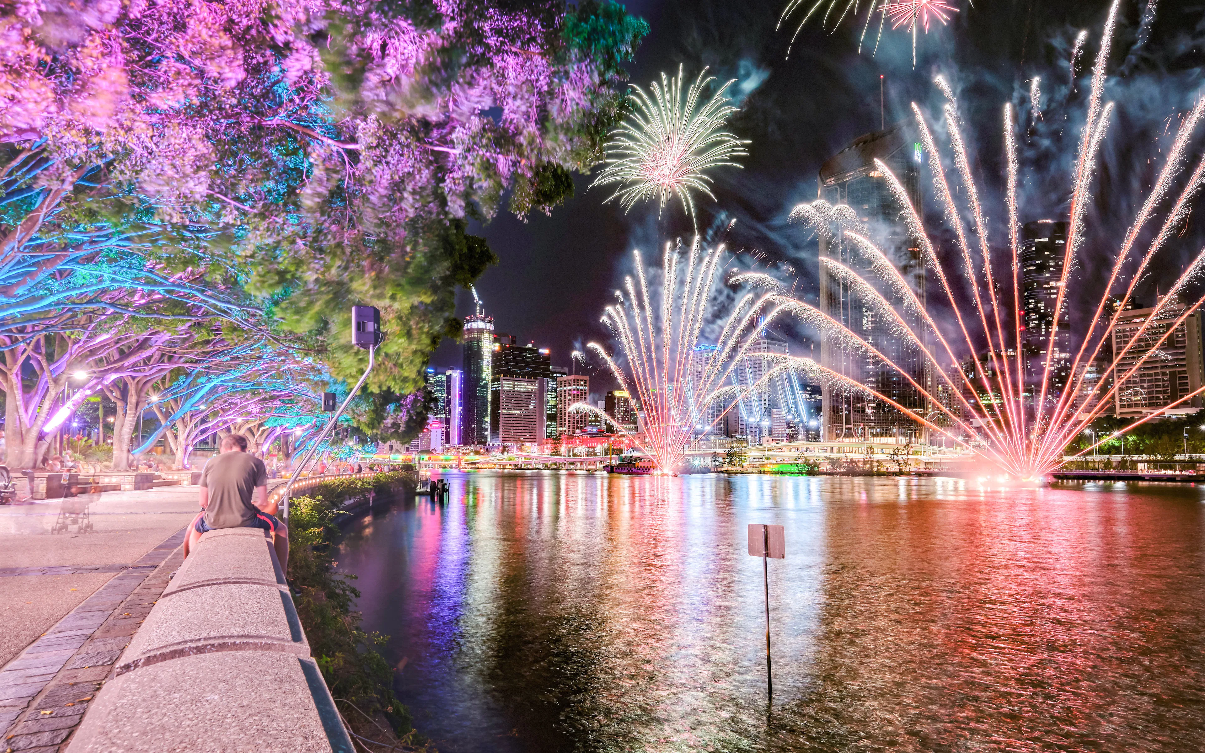 Brisbane River fireworks with colorful trees and people at Southbank during Christmas.