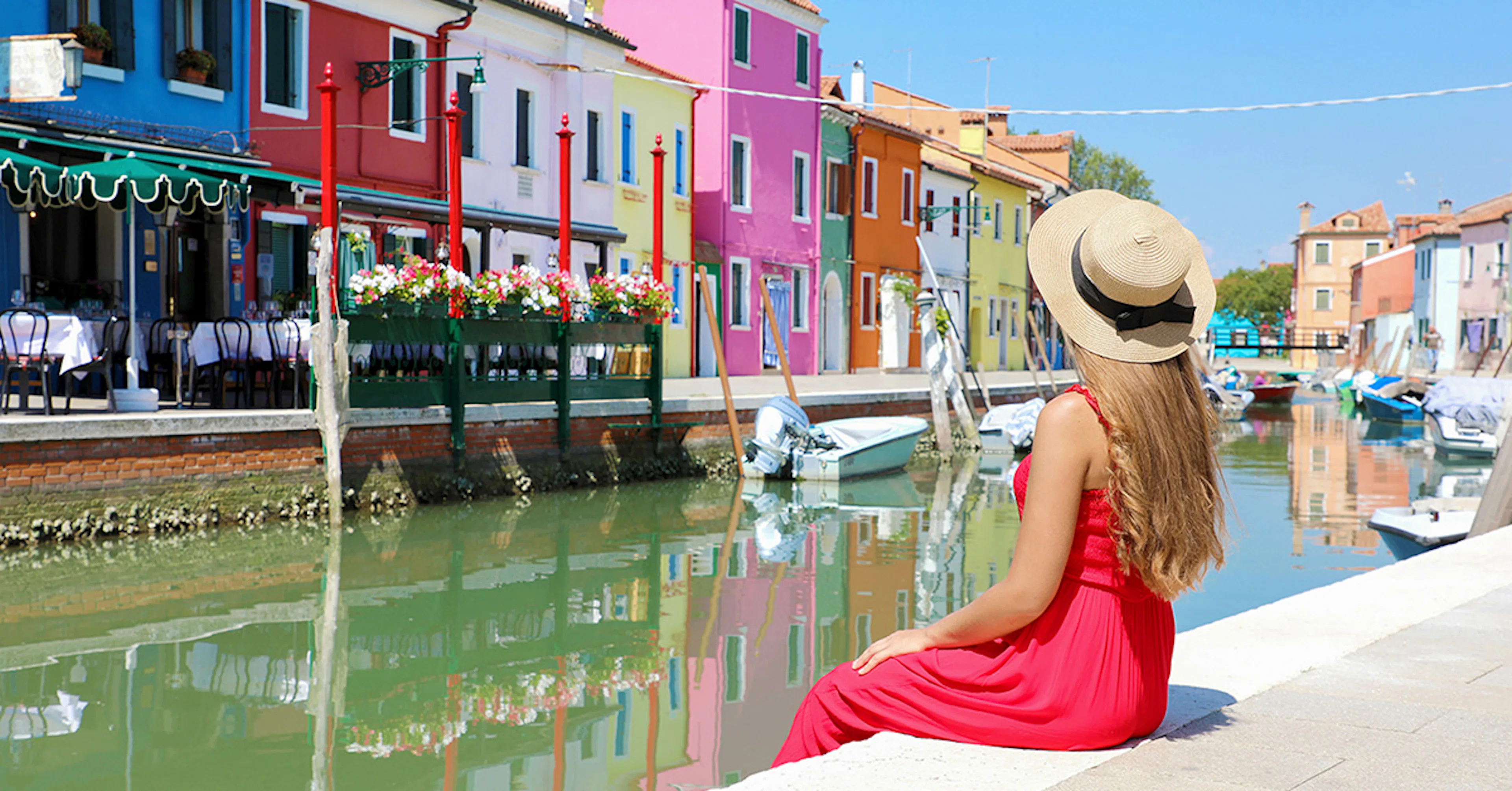 Girl sitting by a canal, admiring colorful buildings in Murano, Italy.