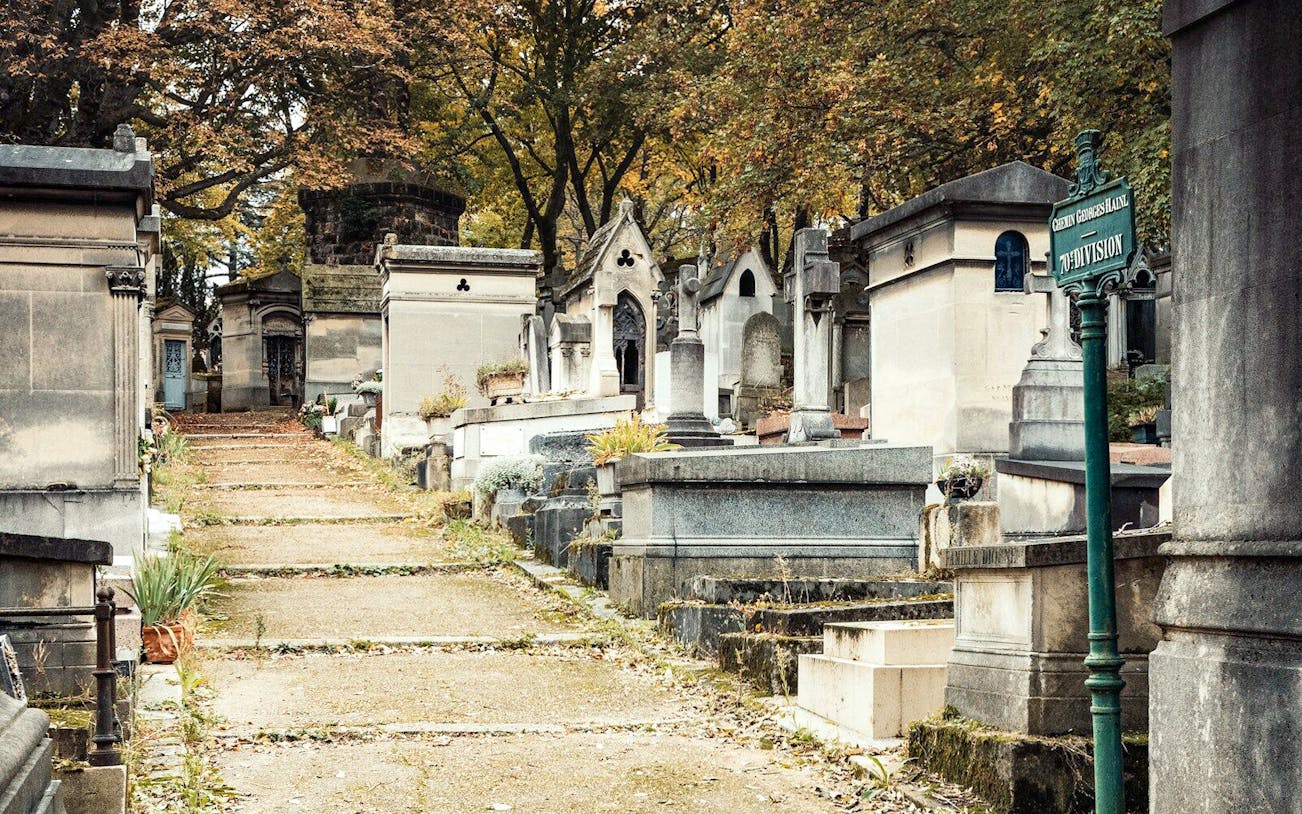 Père Lachaise Cemetery path with historic tombs and autumn trees, Paris.