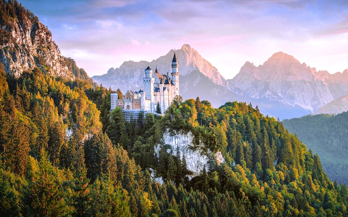 Neuschwanstein Castle surrounded by forested mountains in Bavaria, Germany.