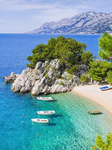 Boats anchored in the clear waters of Blue Lagoon, Croatia, with rocky coastline and distant mountains.