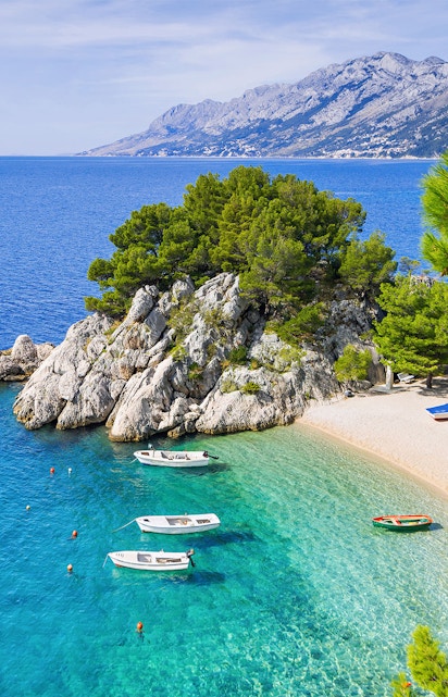 Boats anchored in the clear waters of Blue Lagoon, Croatia, with rocky coastline and distant mountains.
