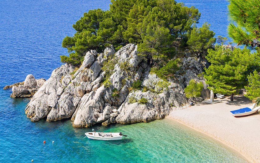 Boats anchored in the clear waters of Blue Lagoon, Croatia, with rocky coastline and distant mountains.