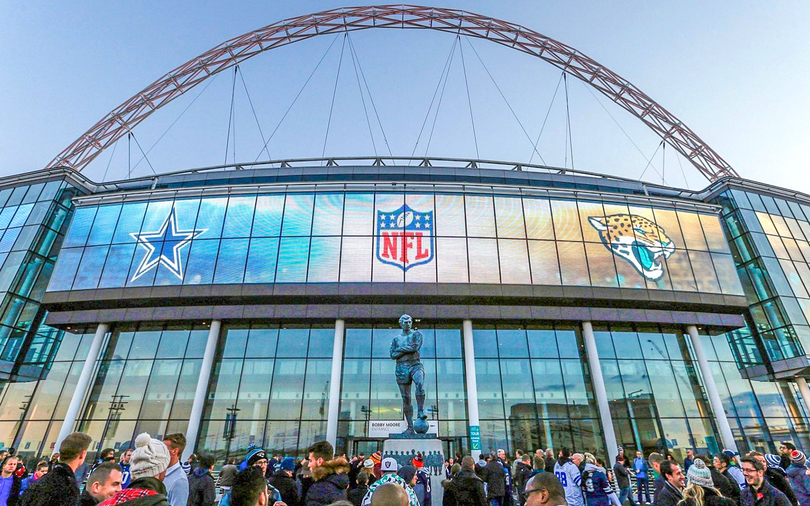 Wembley Stadium exterior with NFL logos and crowd gathering.