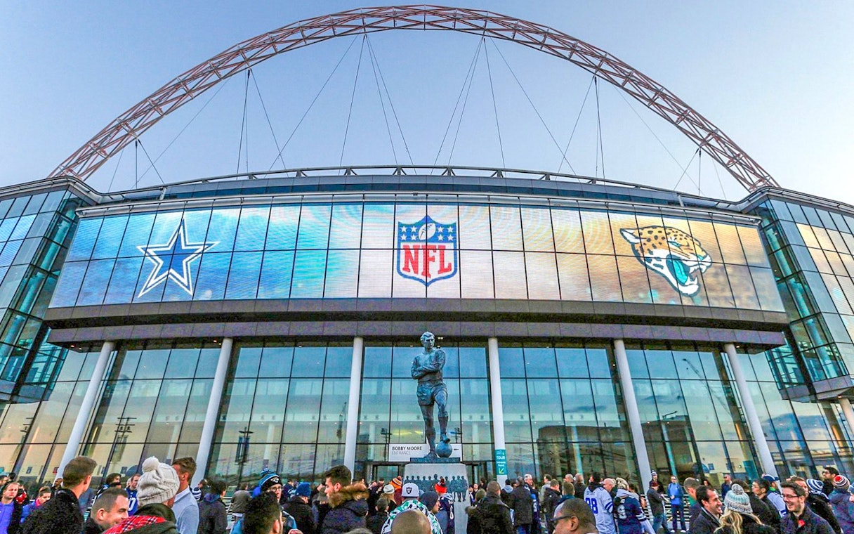 Wembley Stadium exterior with NFL logos and crowd gathering.