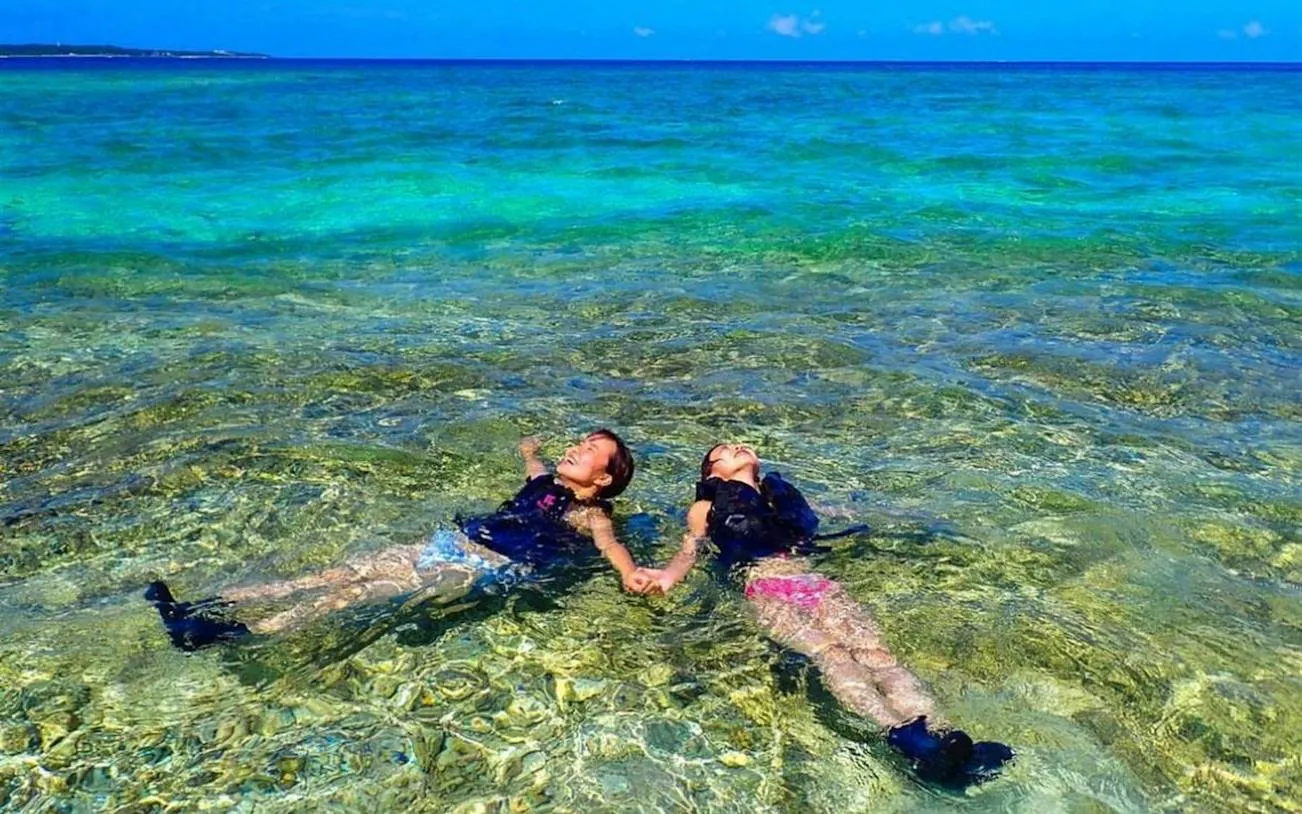 Two people snorkeling at Hoshizuna Beach, Iriomote, Okinawa, with clear turquoise water.