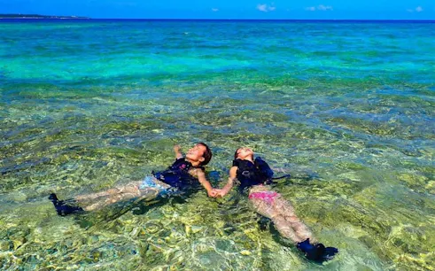 Two people snorkeling at Hoshizuna Beach, Iriomote, Okinawa, with clear turquoise water.