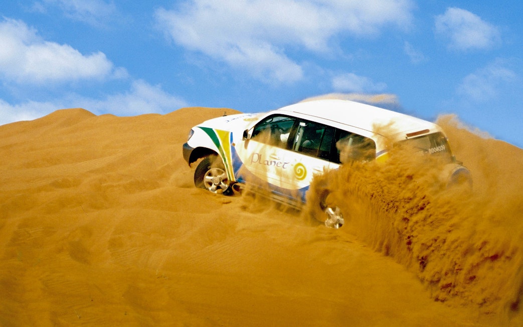 SUV driving through Dubai desert dunes.