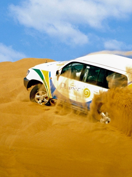 SUV driving through Dubai desert dunes.