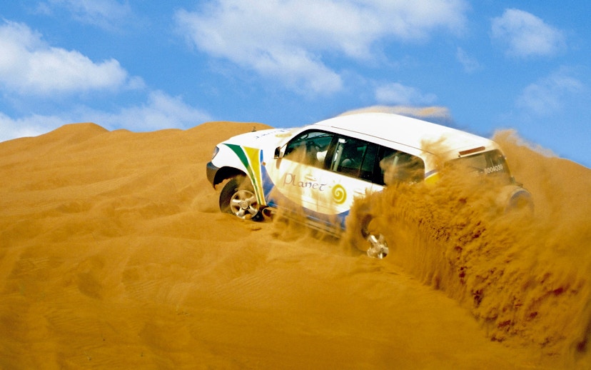 SUV driving through Dubai desert dunes.
