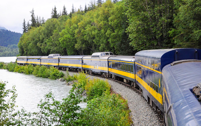 Alaska Railroad train traveling through lush forest along a river.