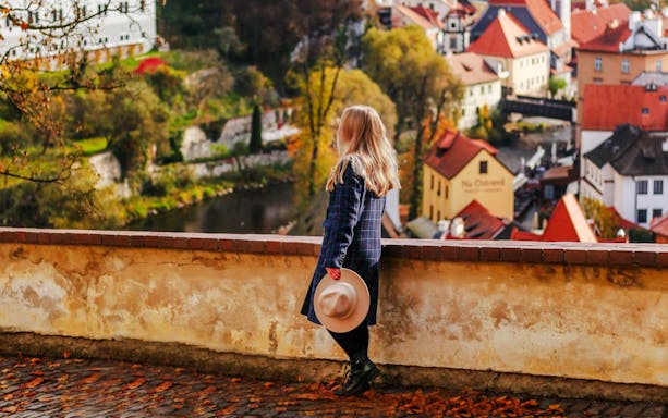 Girl tourist overlooking Cesky Krumlov rooftops and autumn landscape, Czech Republic.