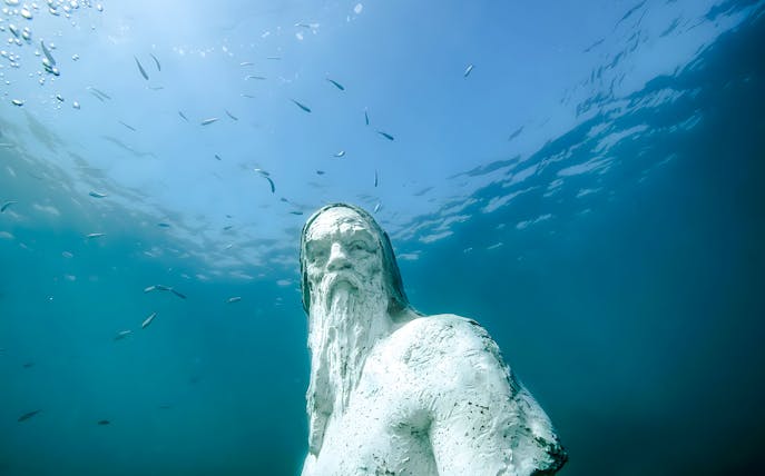 Underwater statue in Marseille's Underwater Museum, surrounded by marine life.