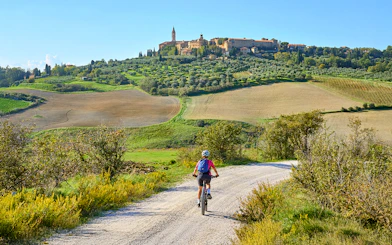 Cyclist on e-bike tour through Tuscan countryside towards hilltop village.