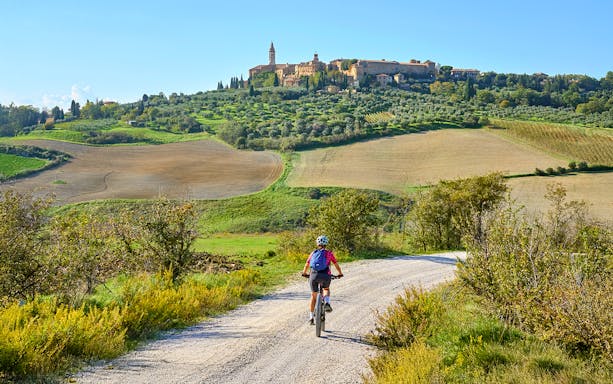 Cyclist on e-bike tour through Tuscan countryside towards hilltop village.