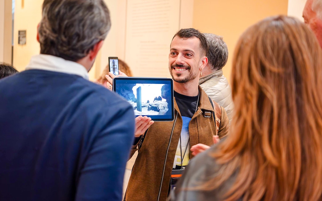 Guide showing tablet to tourists inside Louvre Museum, France.