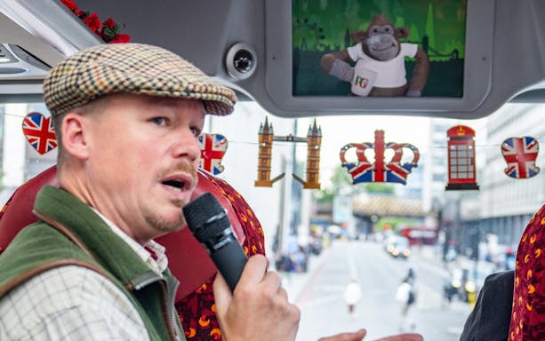 Tour guide speaking on a London sightseeing bus with British-themed decorations.