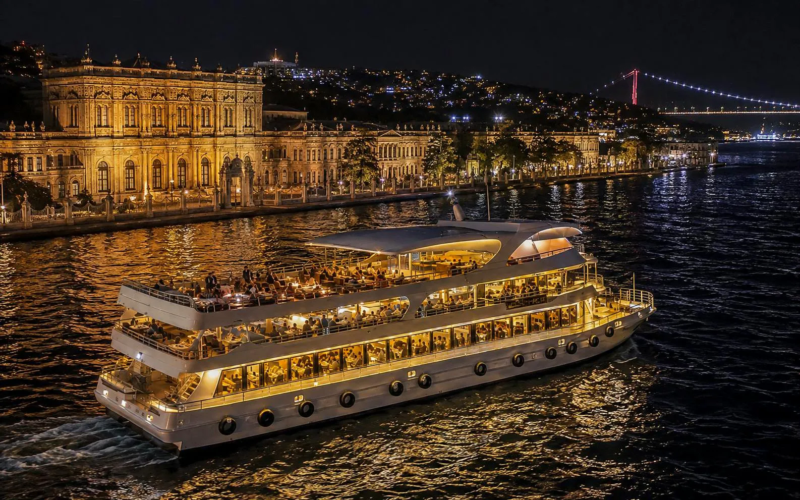 Yacht cruising past Dolmabahçe Palace at night on Bosphorus, Istanbul.