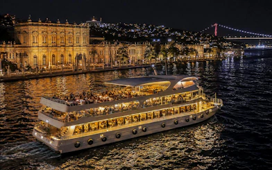 Yacht cruising past Dolmabahçe Palace at night on Bosphorus, Istanbul.