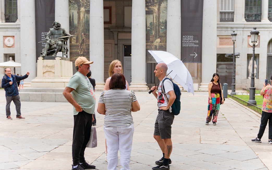 Guide discussing artwork with tourists outside Prado Museum, Madrid.