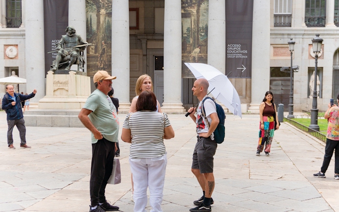 Guide discussing artwork with tourists outside Prado Museum, Madrid.